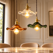 Colorful Glass Copper Edison Pendant Lamp white, orange and green ruffled glass pendant lamps with brass holders glowing above a dining table