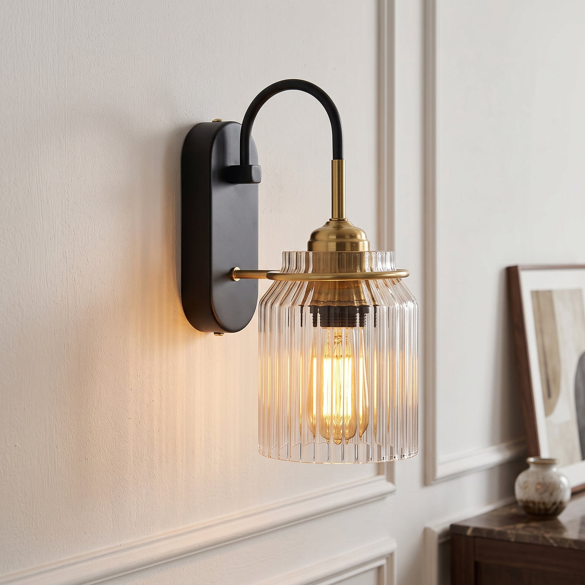 Industrial Style Glass Funnel Wall Lamps black and brass wall sconce with ribbed clear glass shade glowing on a white panelled wall