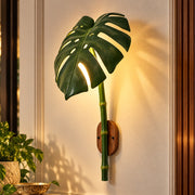 Monstera Leaf Bamboo Outdoor Wall Lamp on a wall beside a plant