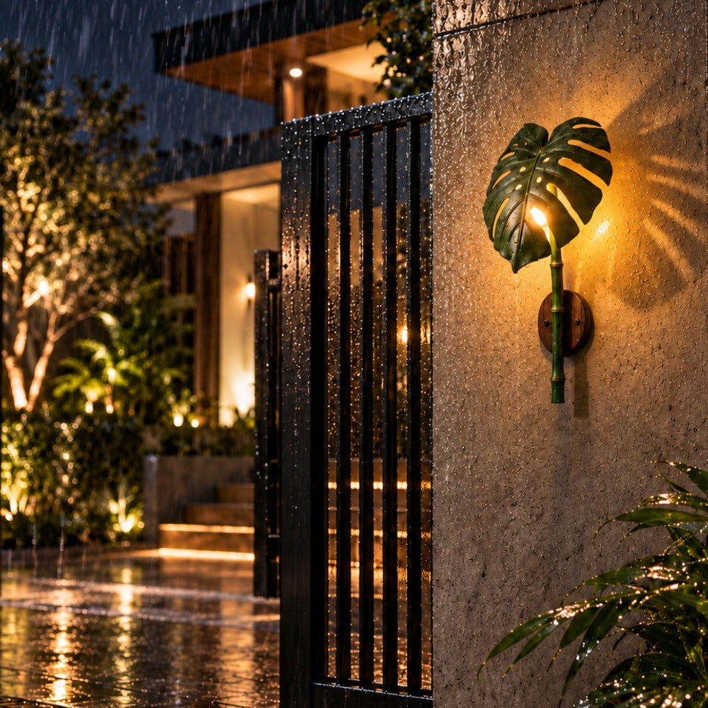 Monstera Leaf Bamboo Outdoor Wall Lamp beside a modern gate at night