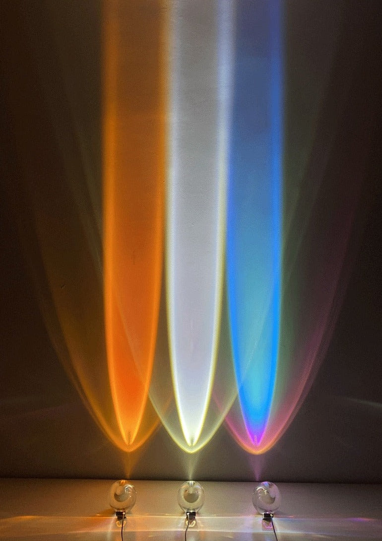 Mystical Radiance Crystal Sky Lamp in Sunset, White and Rainbow casting orange, white and blue light beams up a dark wall